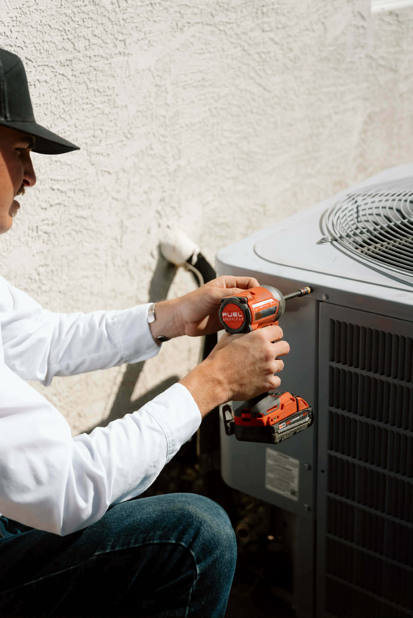 Outlaw Air technician opening the service panel of an outdoor unit with a cordless impact driver