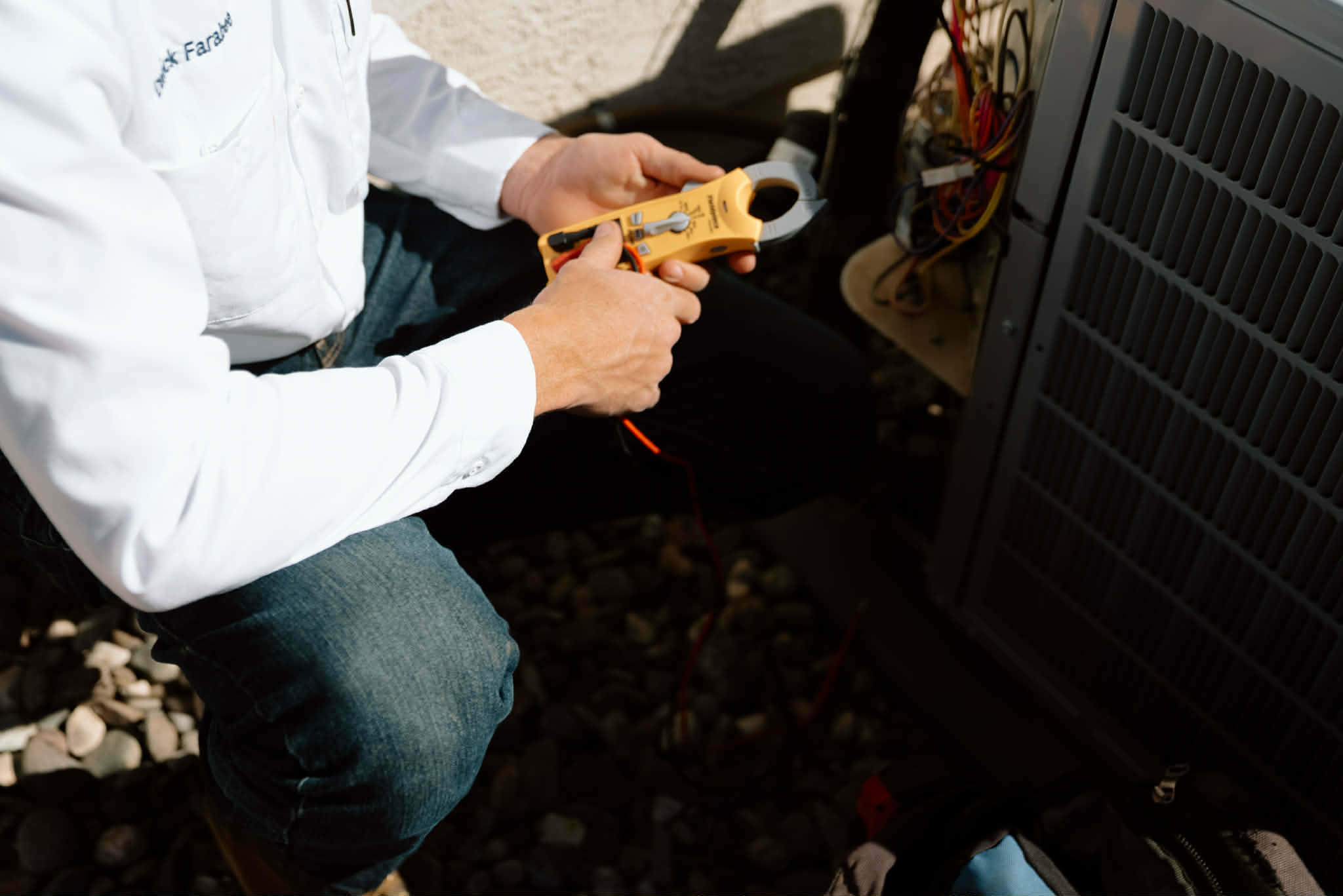 Outlaw Air technician testing the electrical parts of an outdoor AC unit with a clamp meter