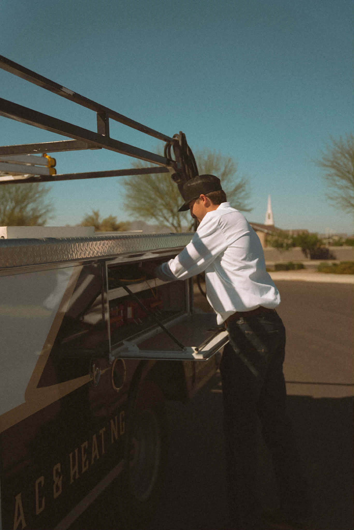 Outlaw Air technician reaching into an open side compartment of the service truck under the ladder rack